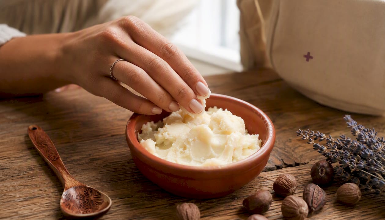 Hand scooping creamy shea butter from jar on linen