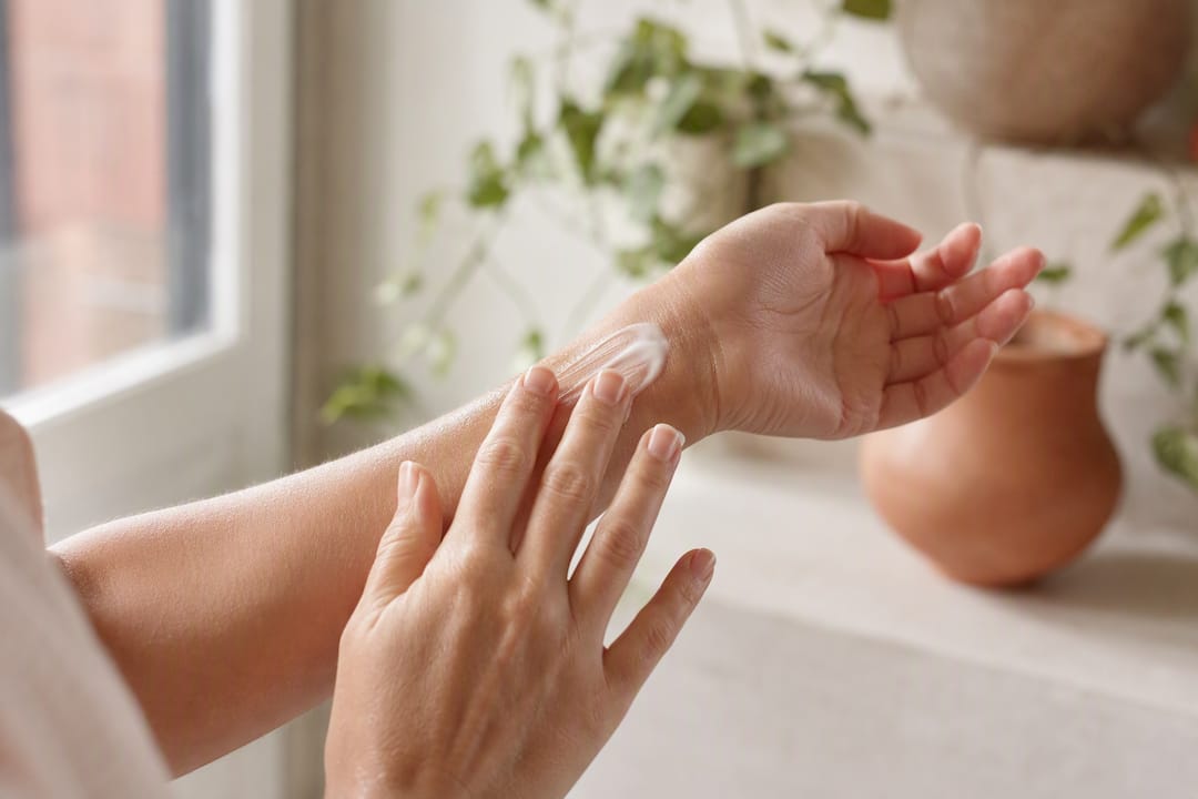 Fingertips patting moisturizer on fragile arm skin