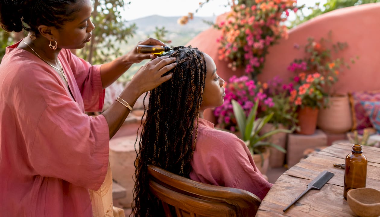 Hands applying oil to boho braid roots gently