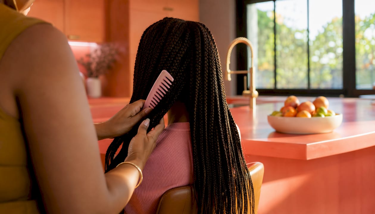 Hands detangling hair with wide-tooth comb over sink