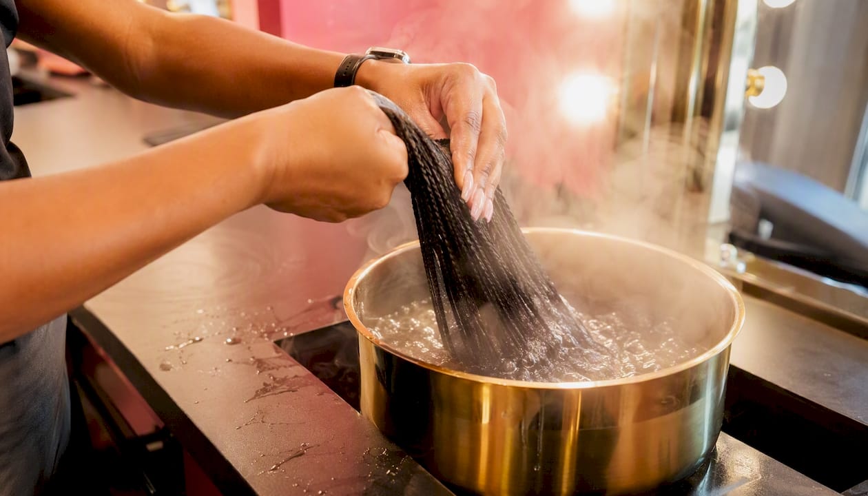 Hands dipping synthetic braiding hair in hot water bowl