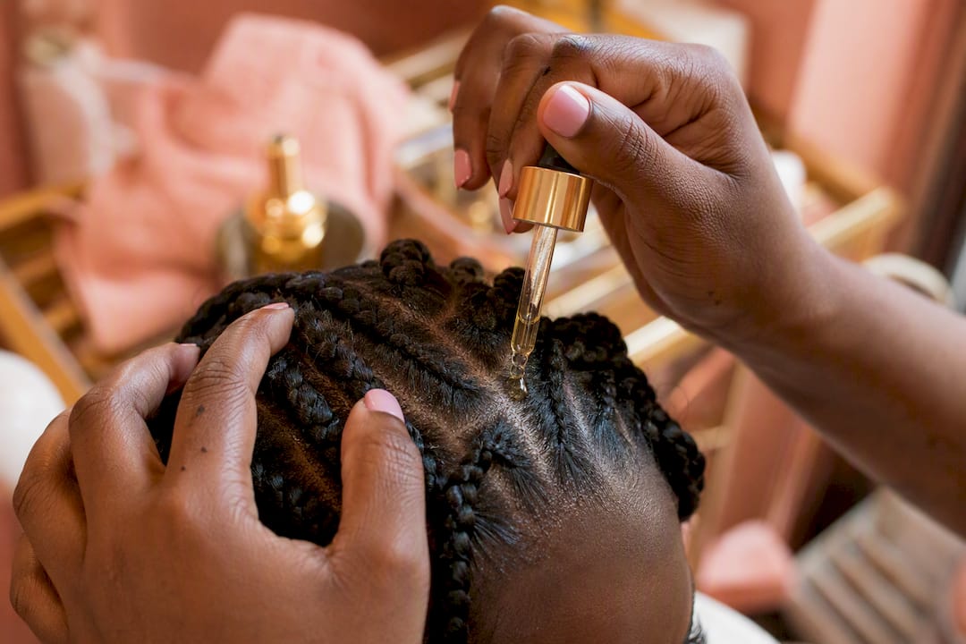 Hand applying medicated scalp oil on scalp near braids