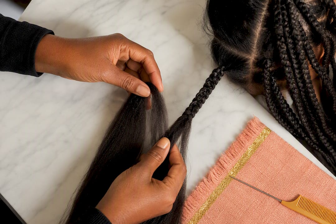 Hands blending hair extensions into braid