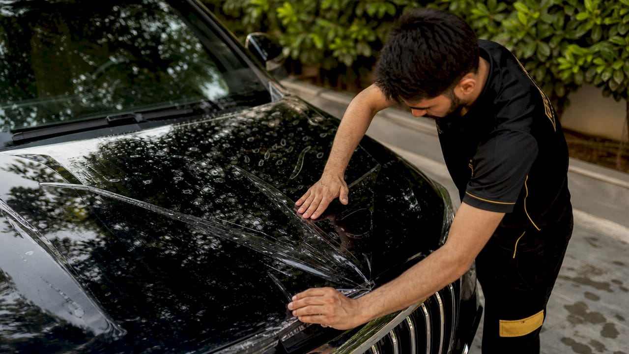 Technician applying paint protection film to car hood