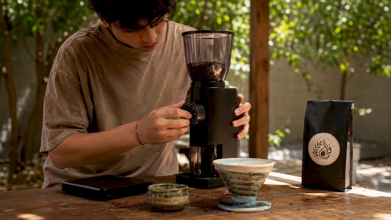 Hands adjusting coffee grinder dial in kitchen