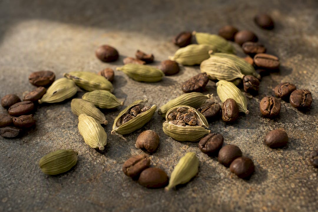 Detalle de vainas de cardamomo verde junto a granos de café