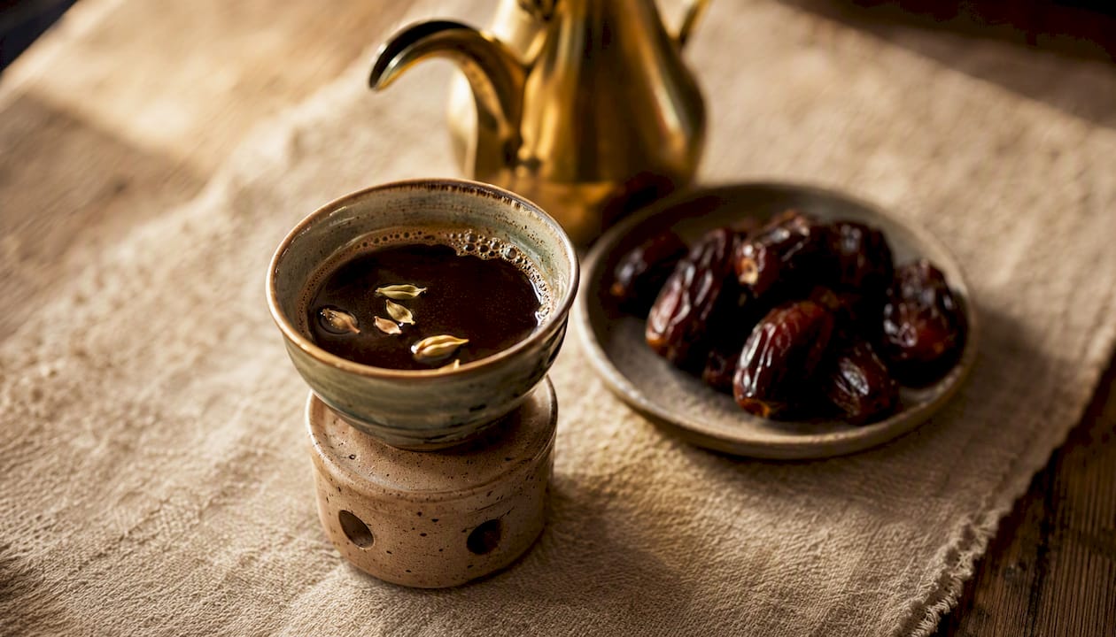 Taza de café árabe acompañada de dátiles y una tradicional cafetera dallah