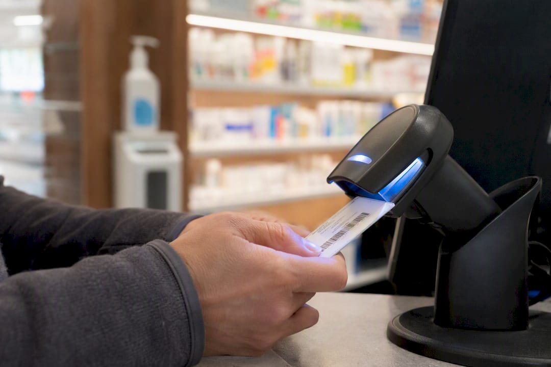 Hands scanning insurance card at pharmacy kiosk