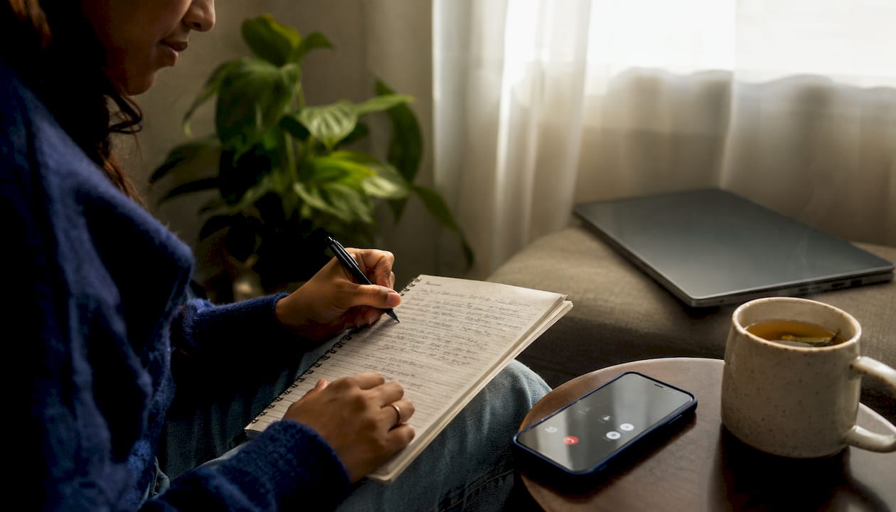 Hands holding smartphone over cluttered desk with planner