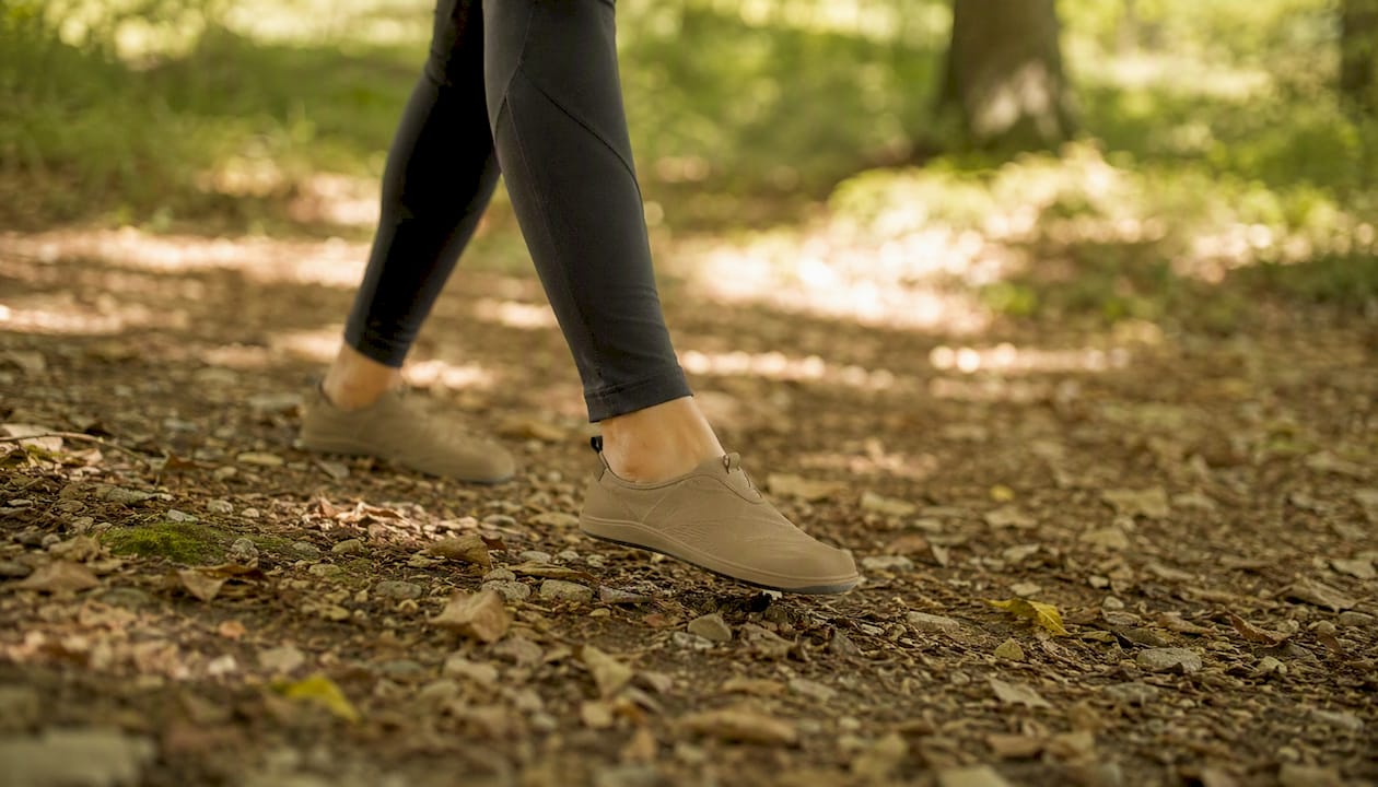 Mit ihren Barfußschuhen spaziert die Person entspannt auf einem Waldweg und genießt die natürliche Umgebung.