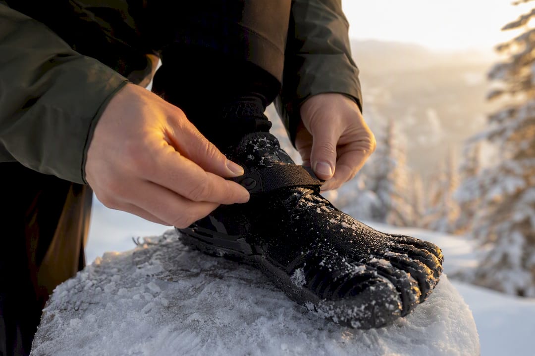 Hände befestigen eine Spikes-Sohle an einem Barfußschuh.