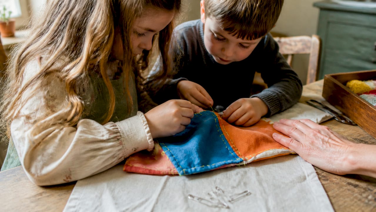 Kinder sitzen an einer Reparaturstation und nähen gemeinsam Stoffe.
