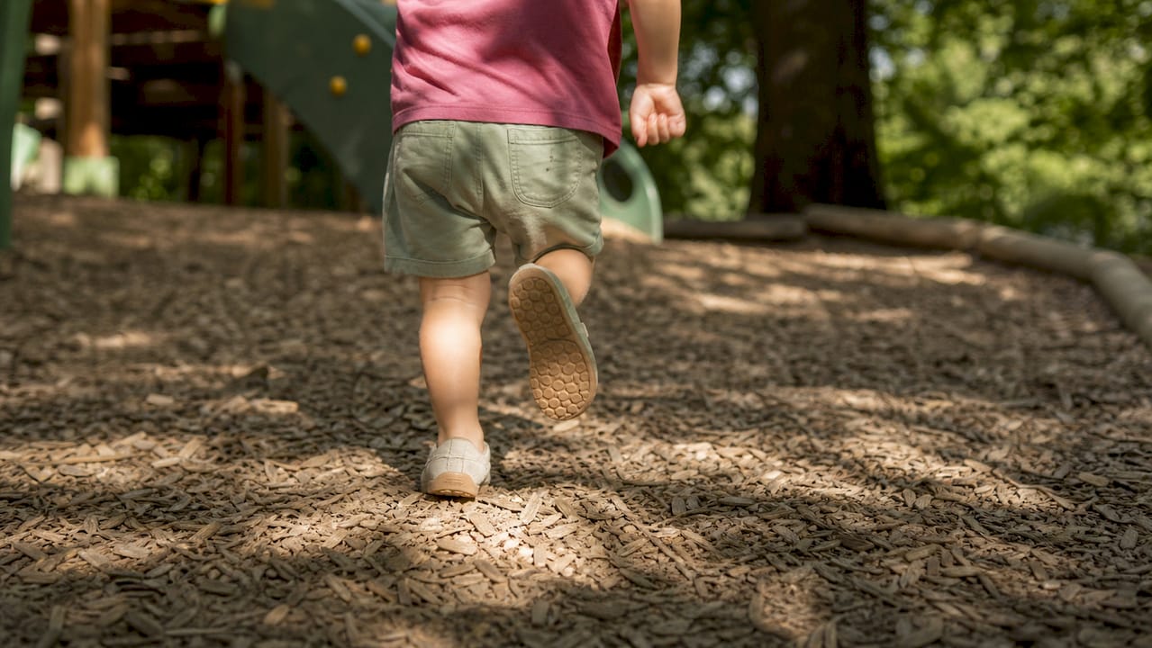 Ein Kind macht seine ersten Schritte in bequemen Schuhen mit breiter Zehenbox, die viel Bewegungsfreiheit bieten.