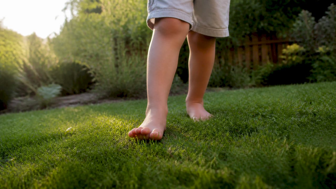 Ein Kind läuft barfuß über das weiche Gras im Garten und genießt die Freiheit und das Gefühl unter den Füßen.