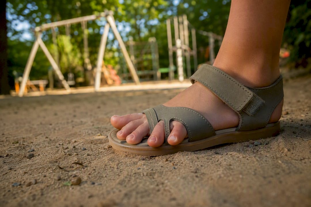 Kinderfuß spreizt die Zehen in einer breiten Sandale