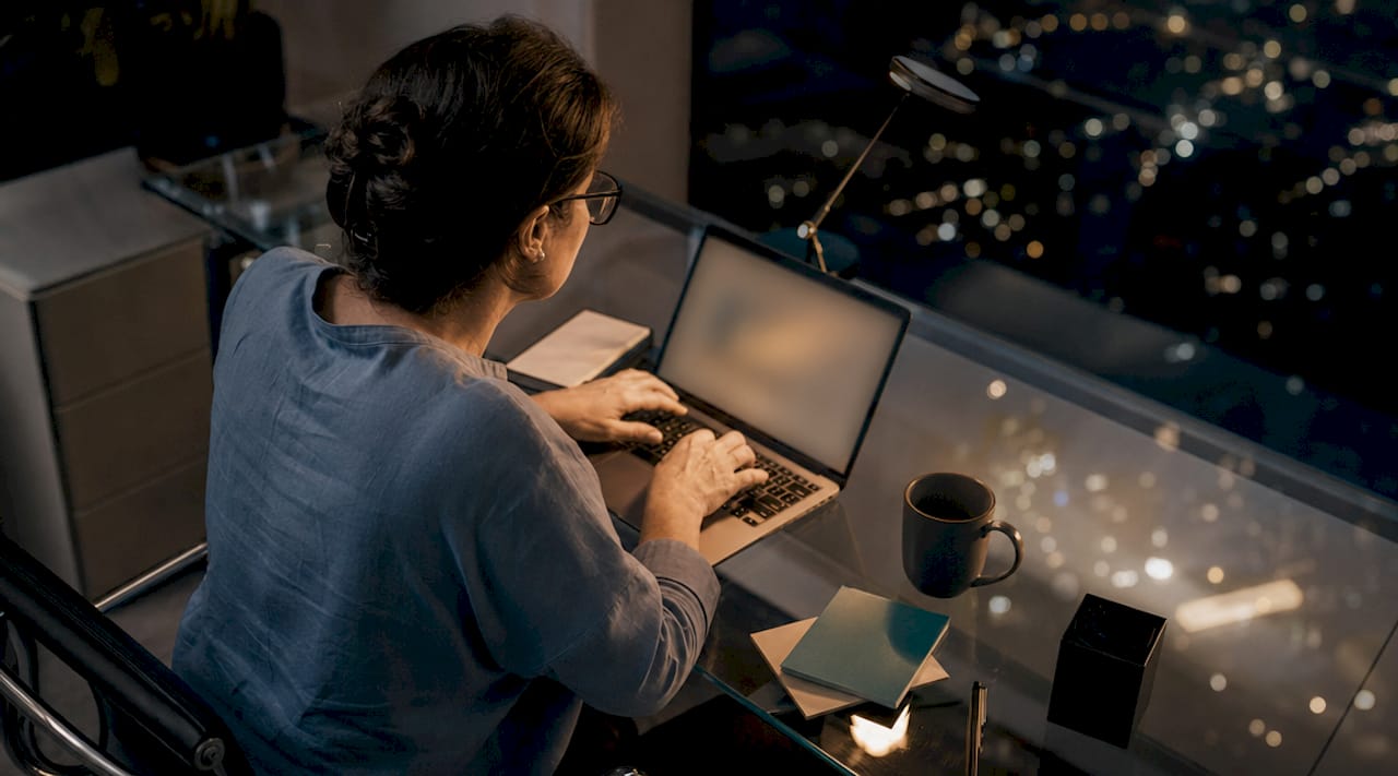 Une femme d’affaires travaille tard le soir à son bureau, échangeant avec un assistant virtuel sur son smartphone.