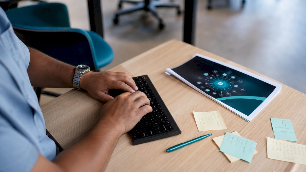 Des mains s'activent sur un clavier, avec un guide d’API posé juste à côté.