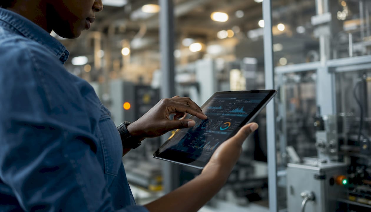 Une technicienne manipule une tablette tactile au cœur d’un environnement industriel.