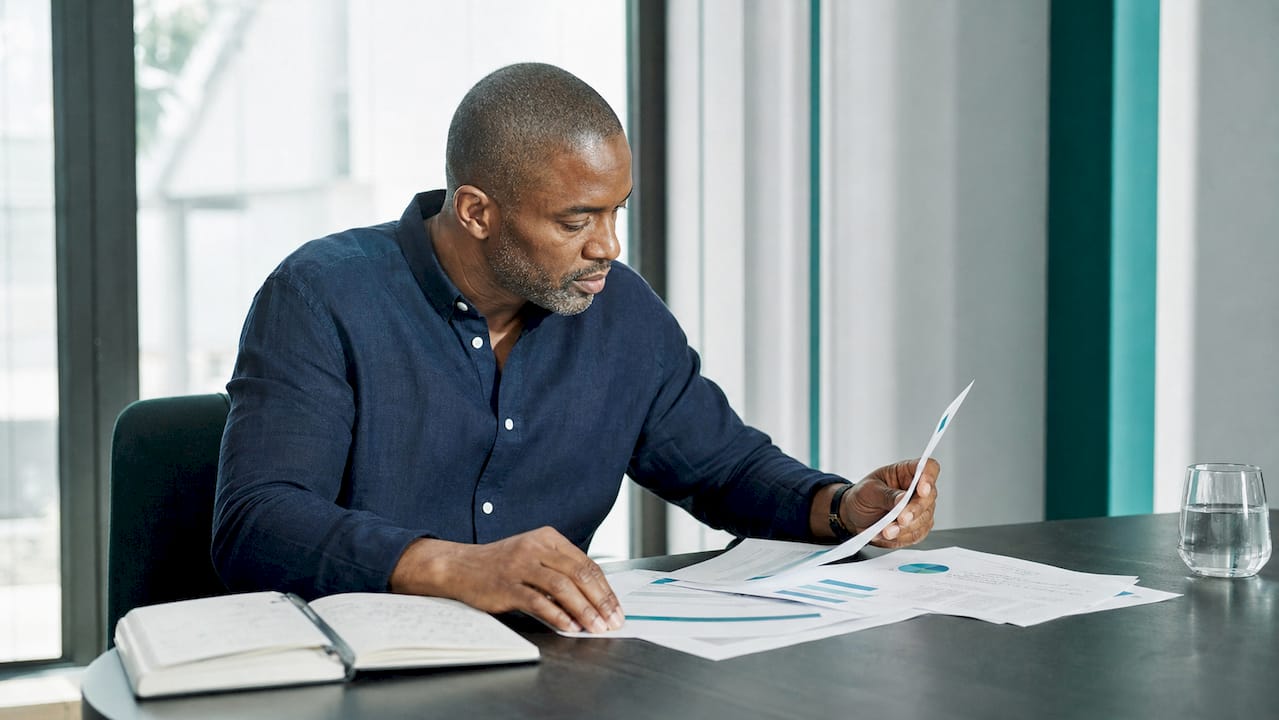 Un homme examine attentivement des documents relatifs à la gouvernance de l’intelligence artificielle, installé à son bureau.