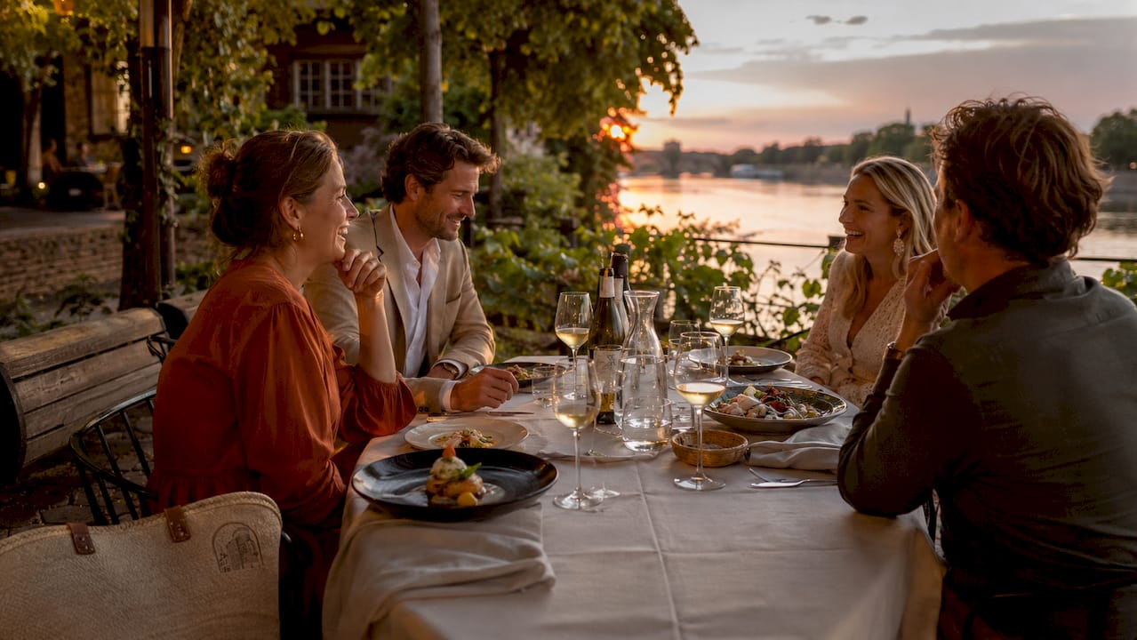 Een groep vrienden geniet samen van een gezellig diner bij restaurant CINQ, met uitzicht op de rivier en smaakvol opgediende gerechten voor zich.