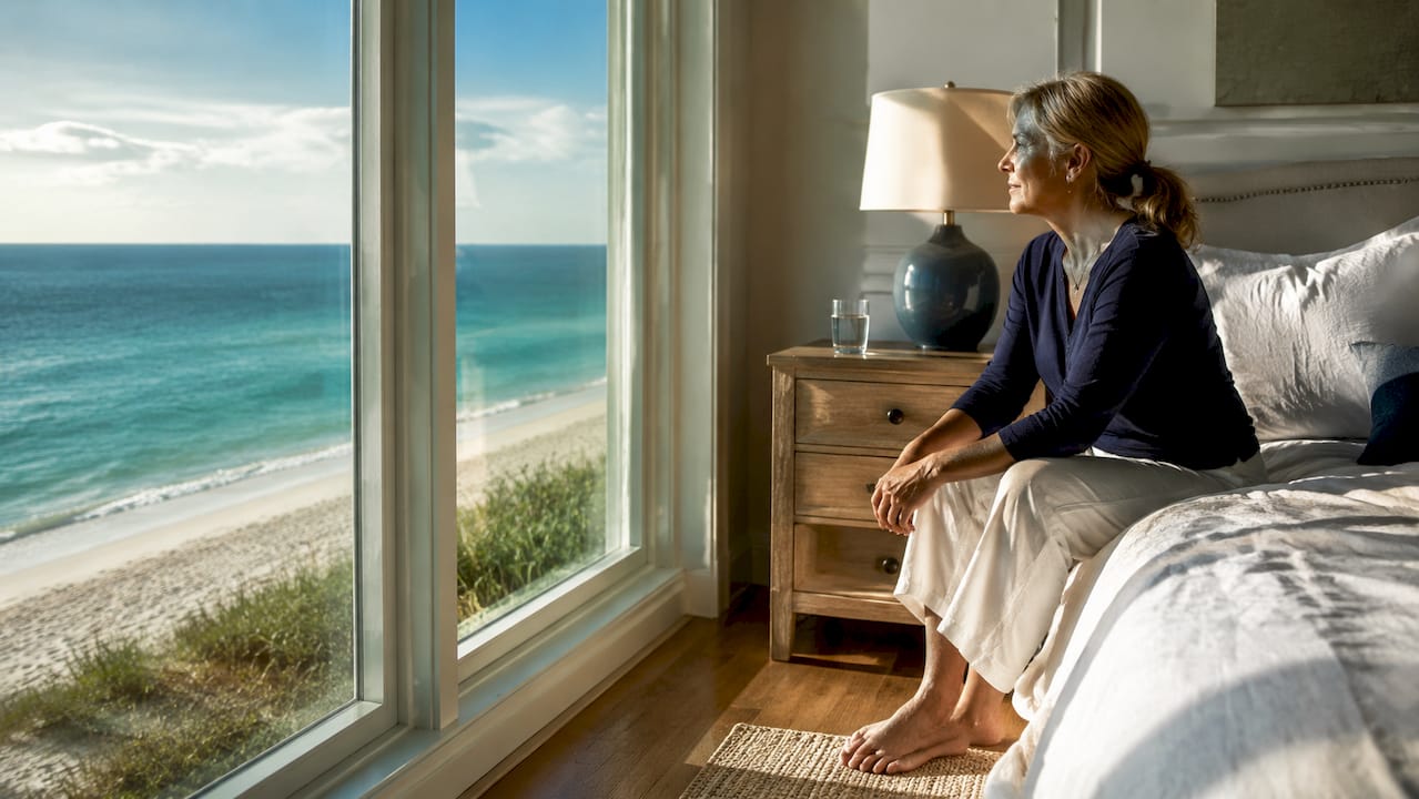Woman sitting on bed looking at oceanfront view