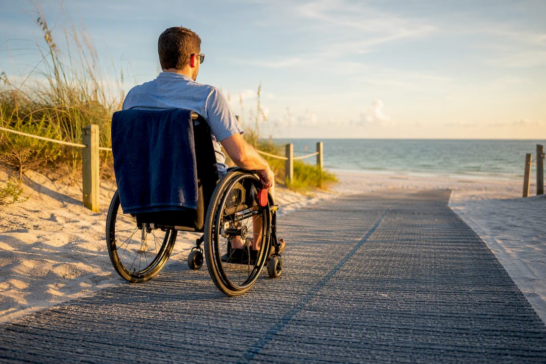 Wheelchair user crossing beach access mat