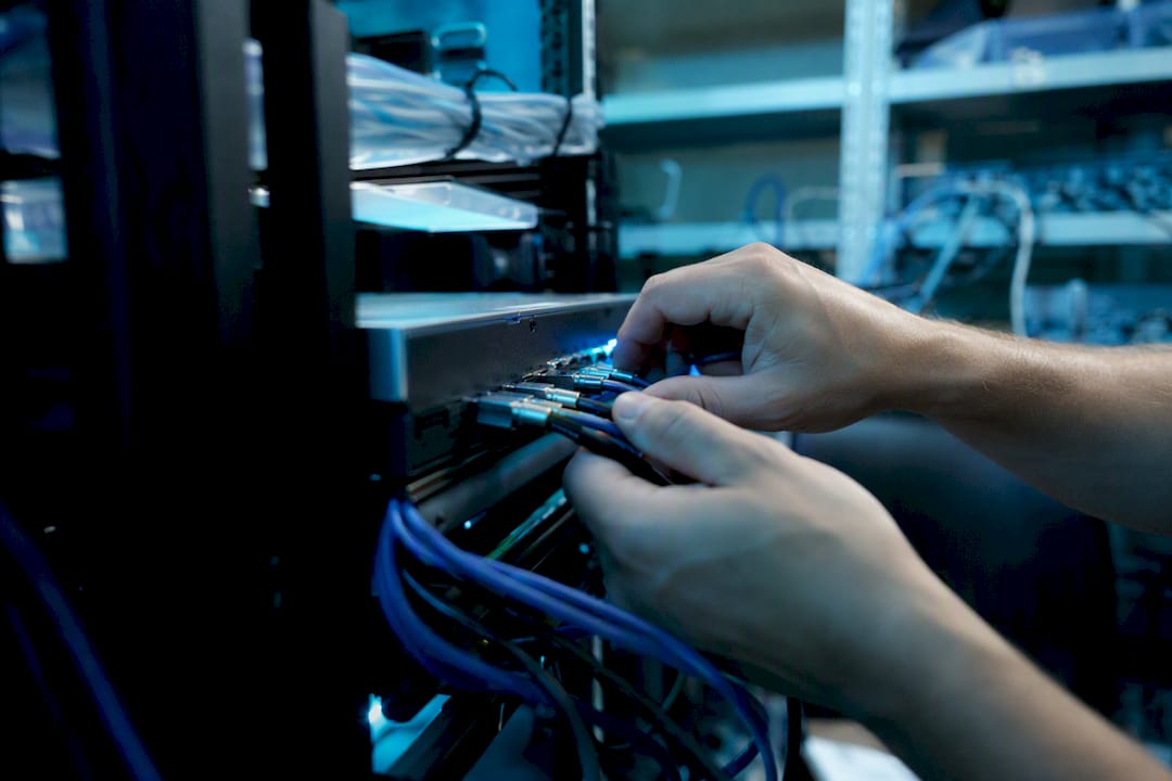 Hands connecting fiber optic cables in server rack