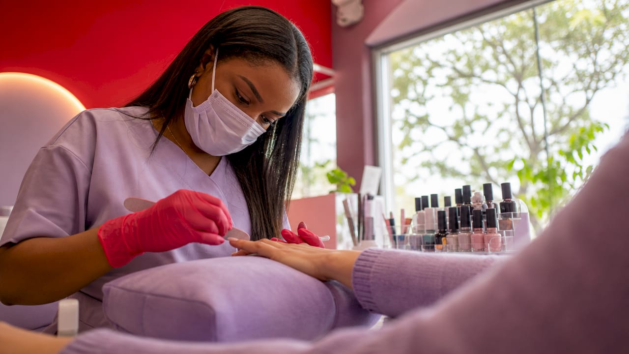 Nail technician filing client's nails in salon