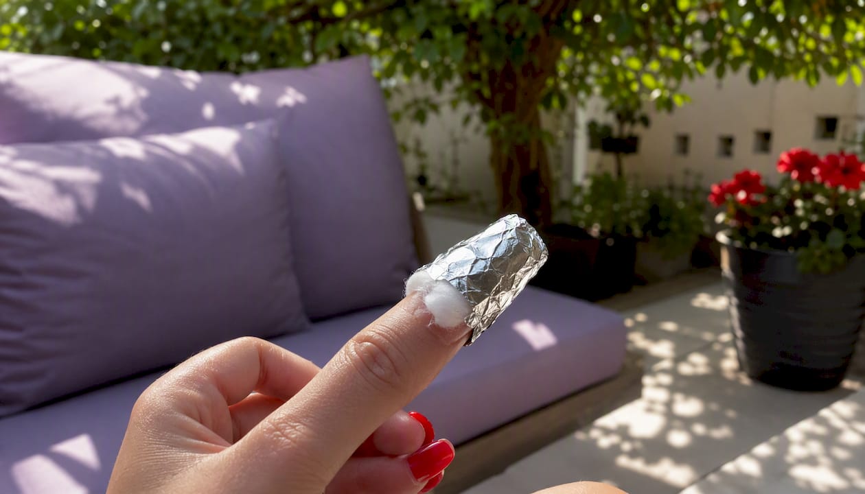 Finger wrapped in foil with acetone-soaked cotton for nail wrap removal