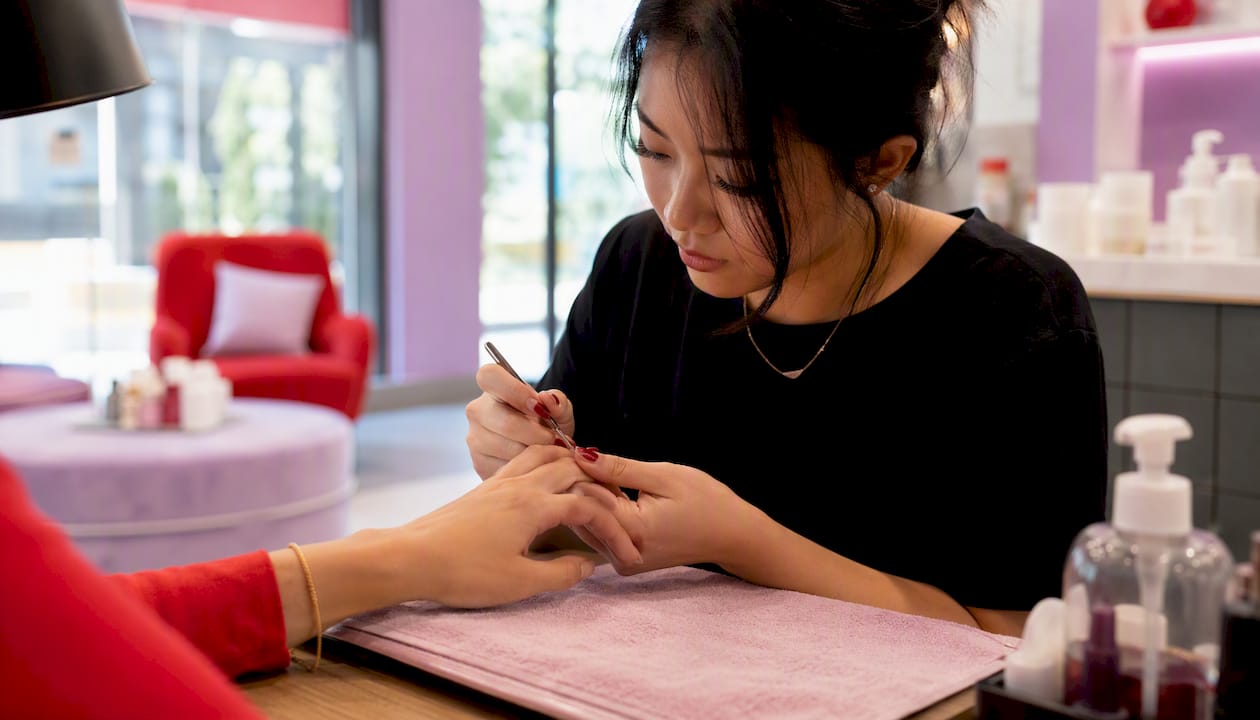 Certified nail technician filing nails at salon