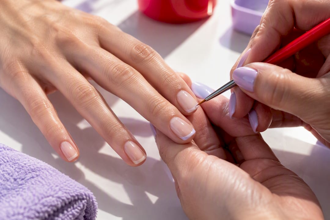 Technician painting a minimalist micro-French nail