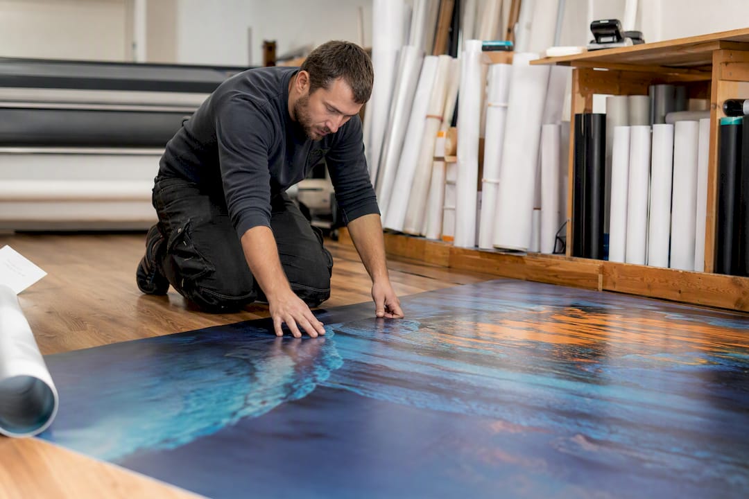 Hands installing large-format floor graphic in workshop