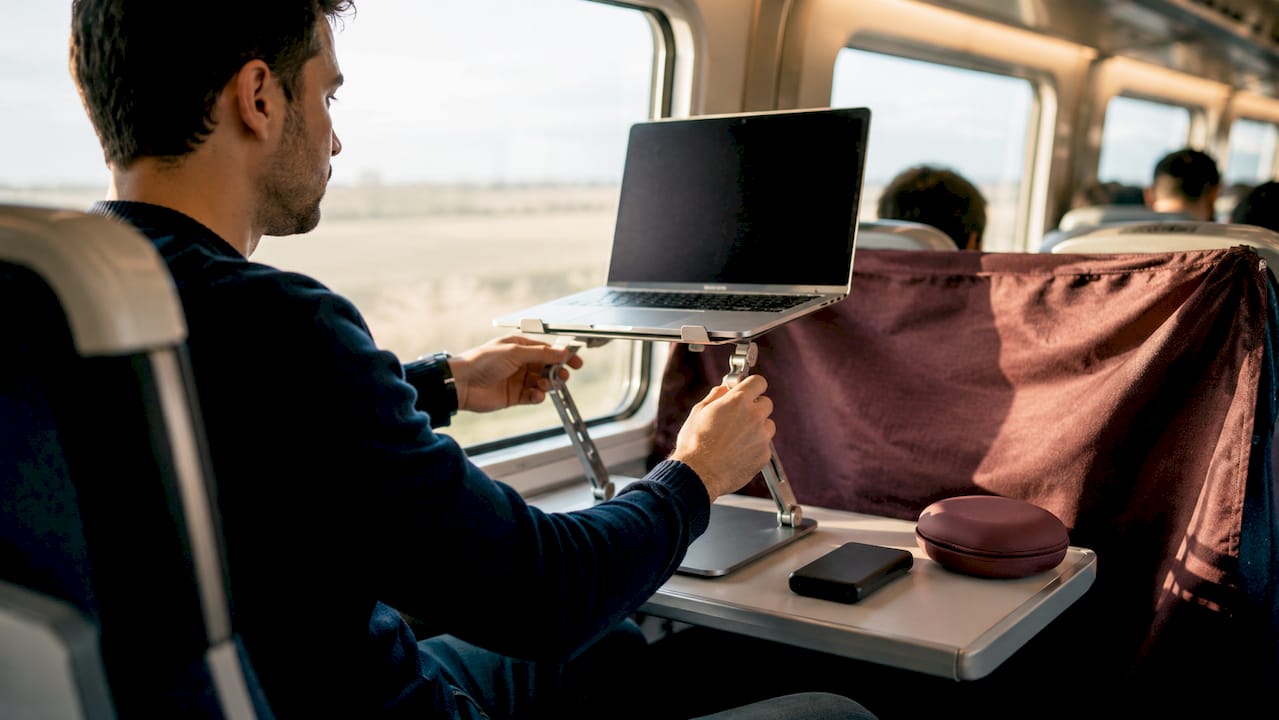 Hands adjusting laptop stand with MacBook on train