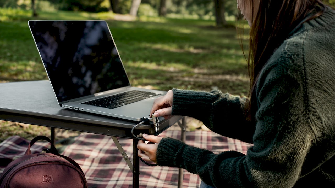 Manos bloqueando una laptop con cable de seguridad en una cafetería