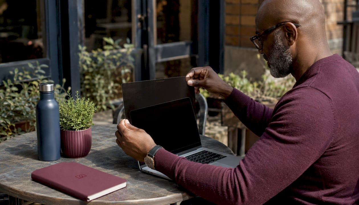 Hands holding adhesive privacy screen near MacBook