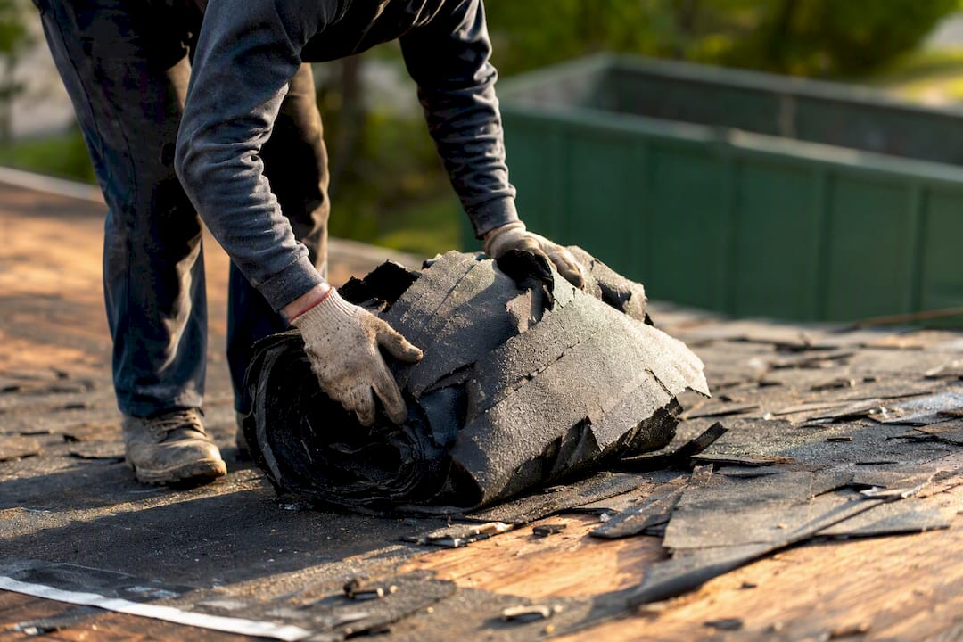 Hands removing old shingles during roof tear-off