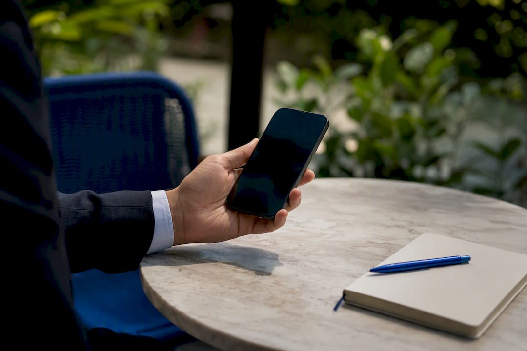 Hand holding smartphone with off screen on bench