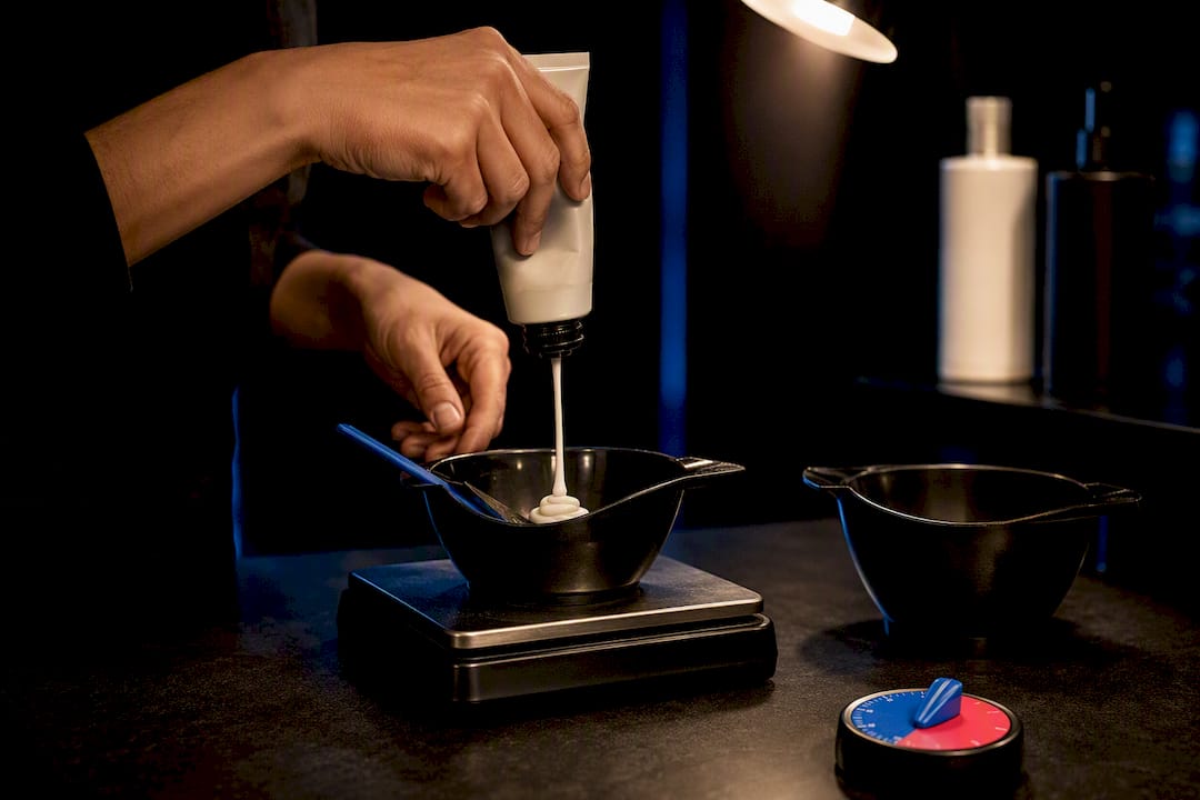 Colorist weighing hair color beside processing timer