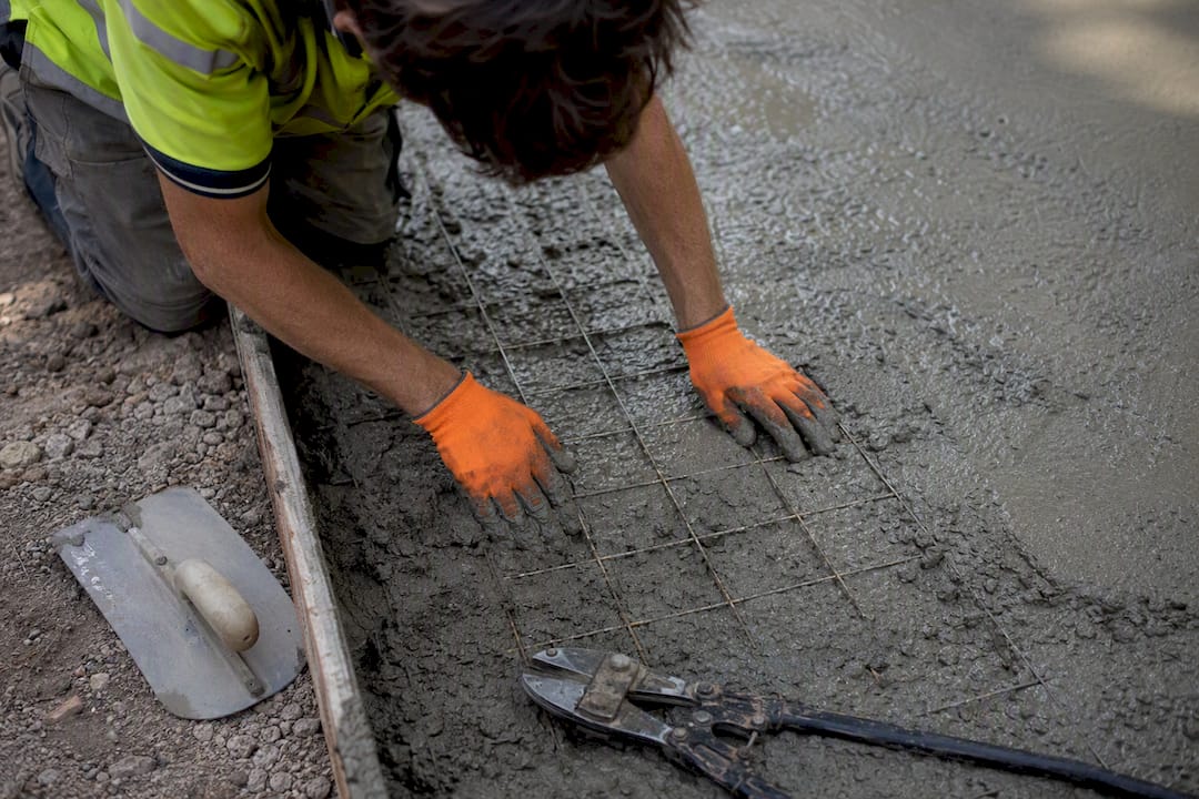 Hands placing welded wire mesh reinforcement in concrete