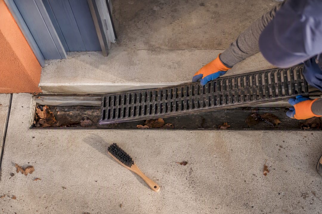 Worker clearing a sloping driveway drain
