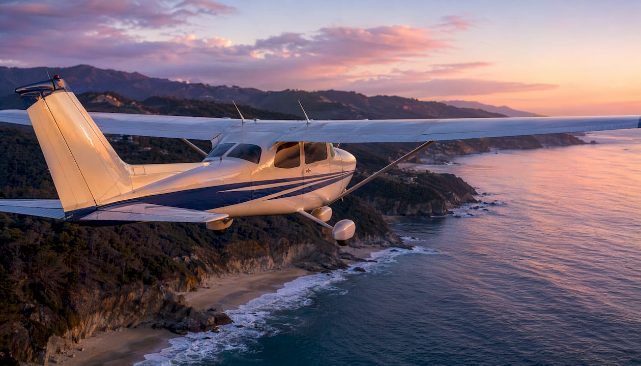 Small aircraft flying along sunlit coastal shoreline