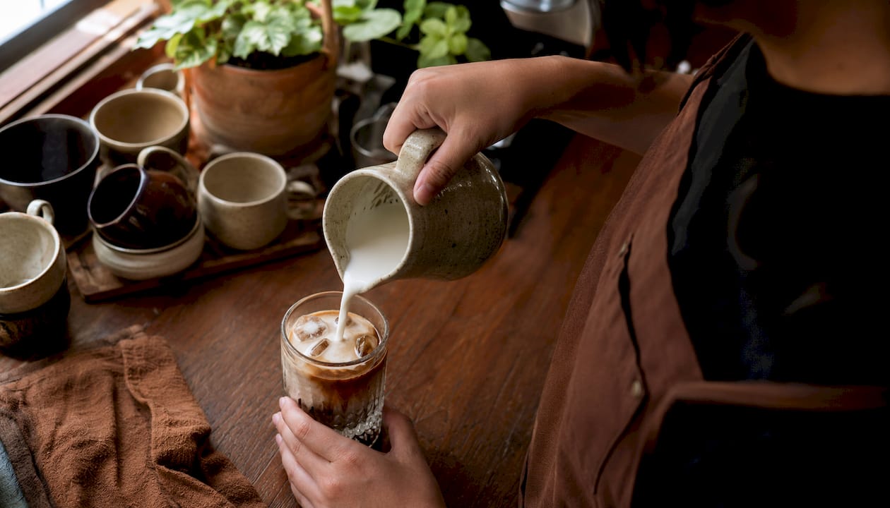 Barista pouring milk over espresso in iced latte