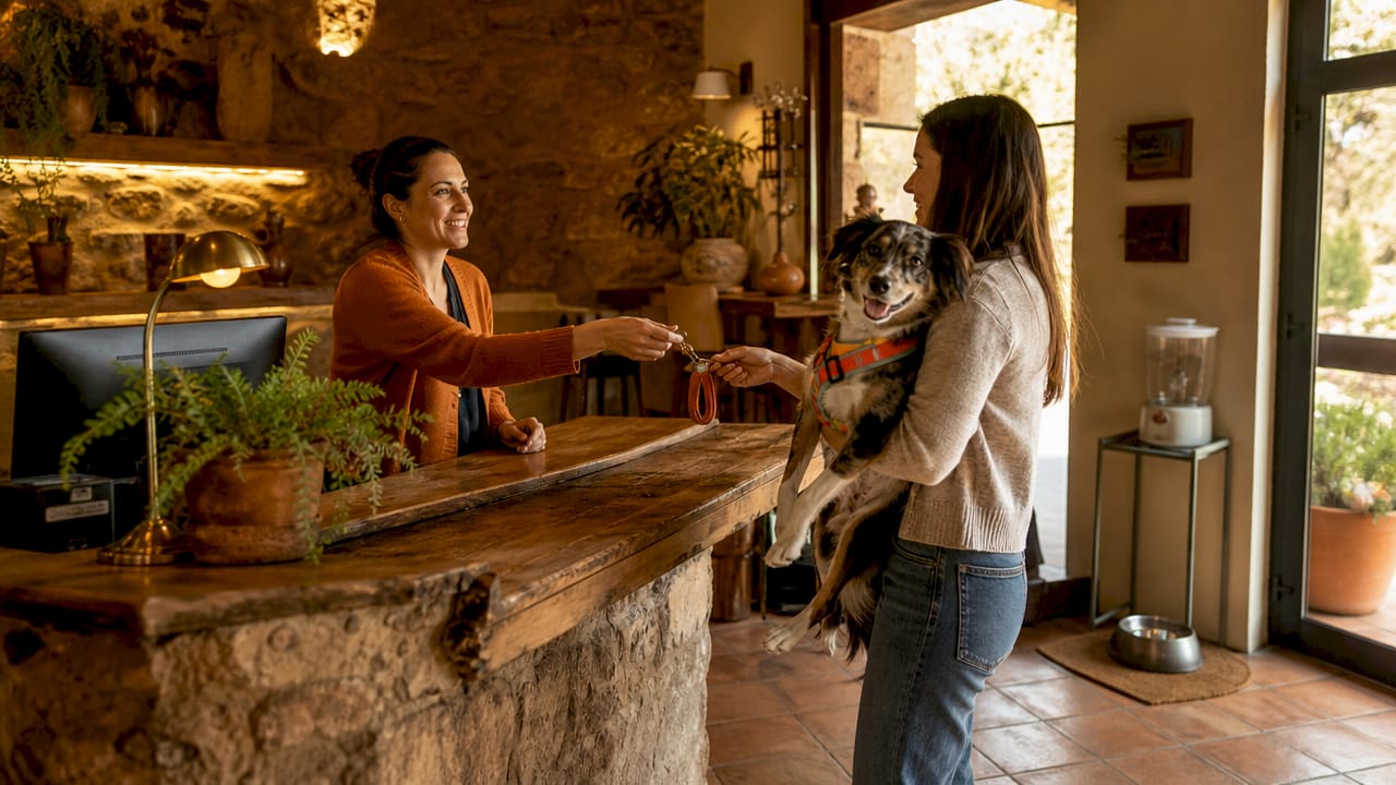 Recepcionista entregando la llave de la habitación a un huésped acompañado de su perro