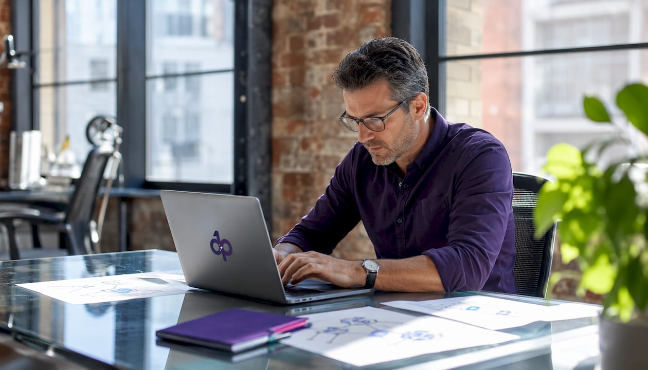 Hands typing on laptop with compliance architecture documents