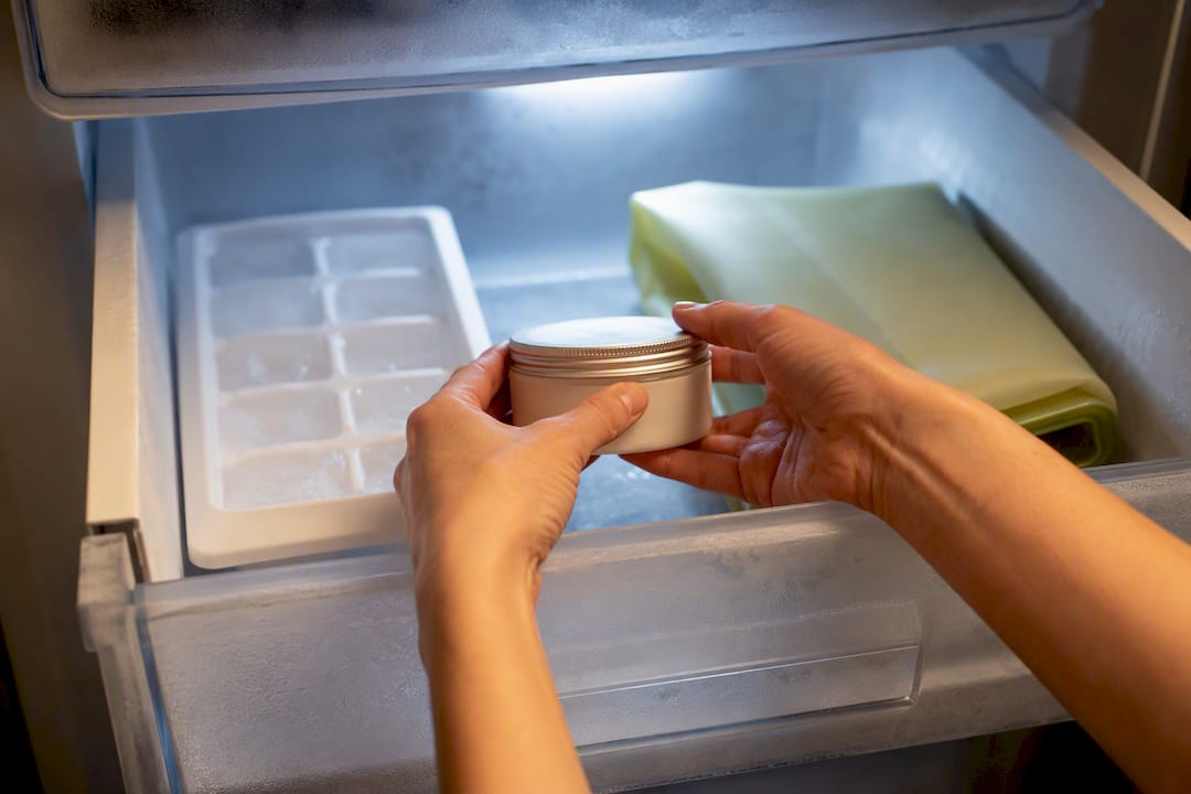 Hands storing anonymous body butter jar freezer