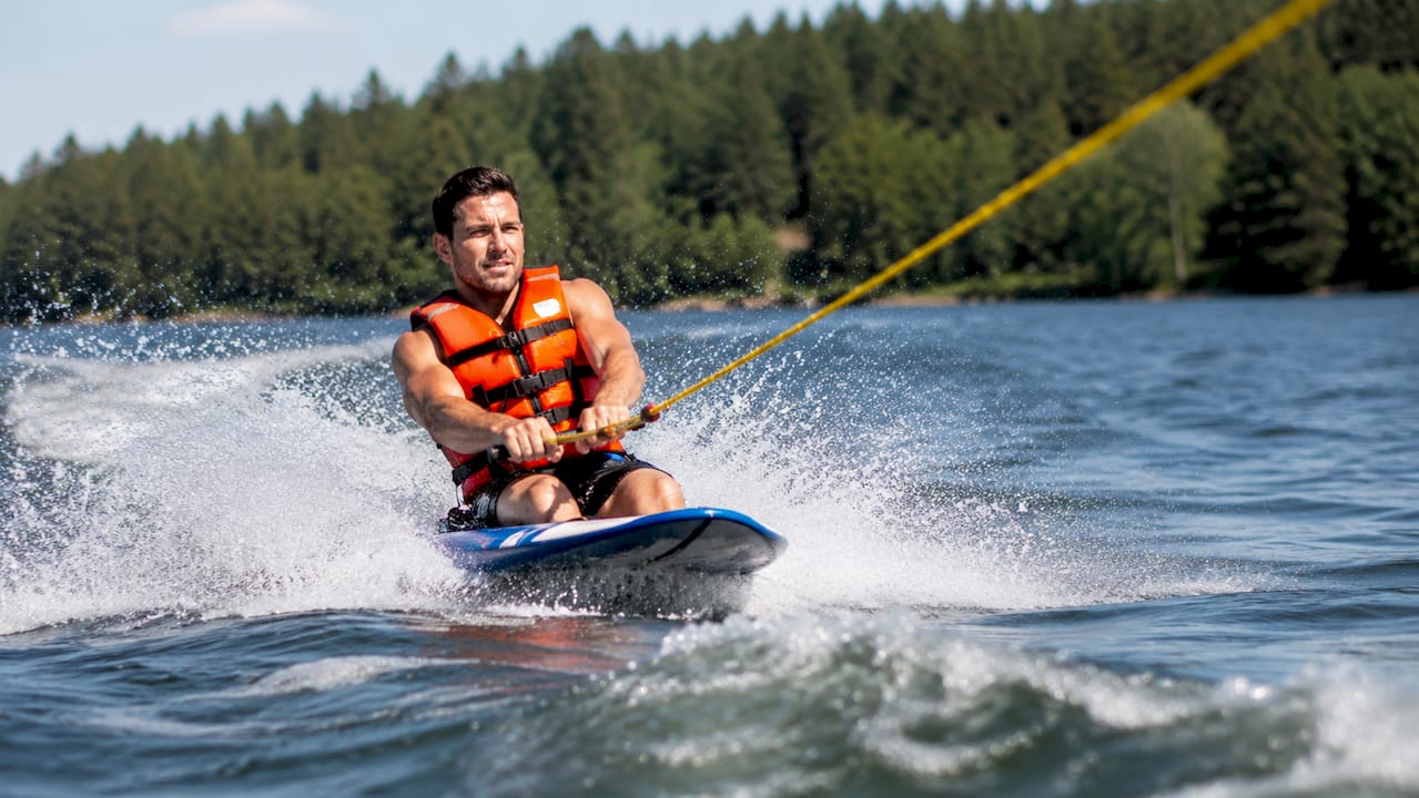 Man kneeboarding behind motorboat on lake