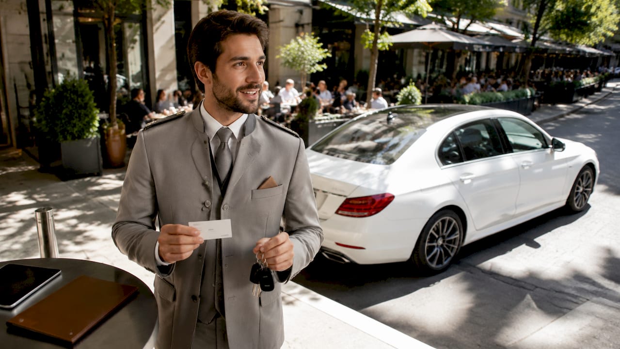 Valet attendant holding concierge parking ticket by luxury car