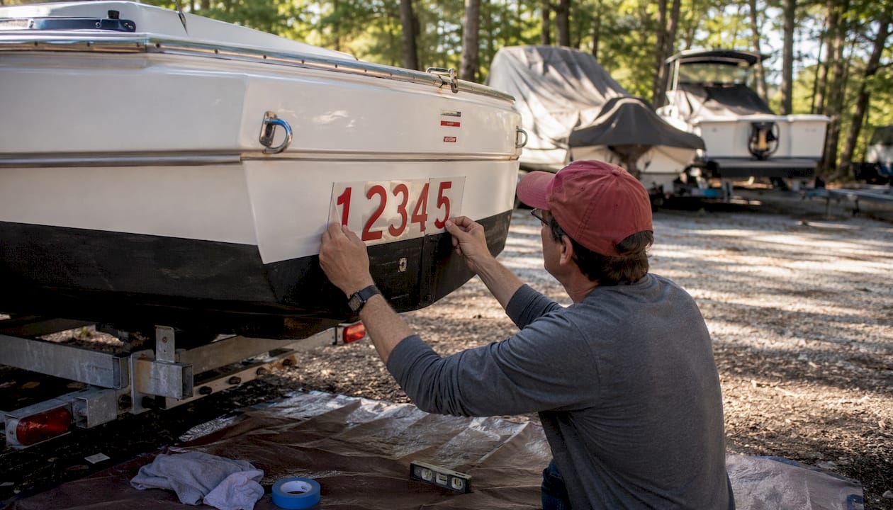 Hands applying registration numbers on sailboat bow