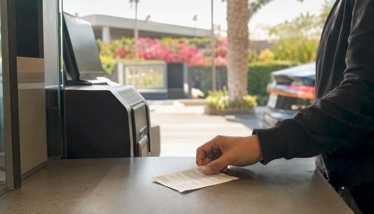 Hand placing multilingual parking ticket in valet booth