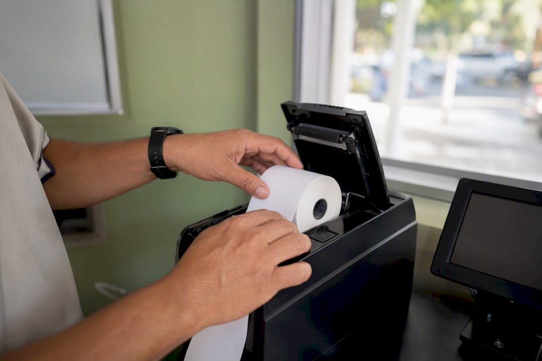 Hands loading thermal ticket roll in parking booth